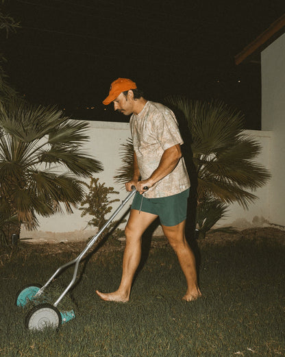 Person using a lawn mower at night in a garden with palm trees.