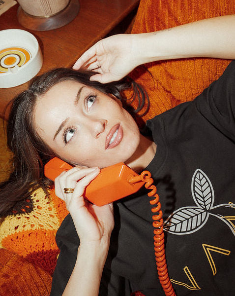 Woman lying on a red couch holding an orange phone in a cozy room.