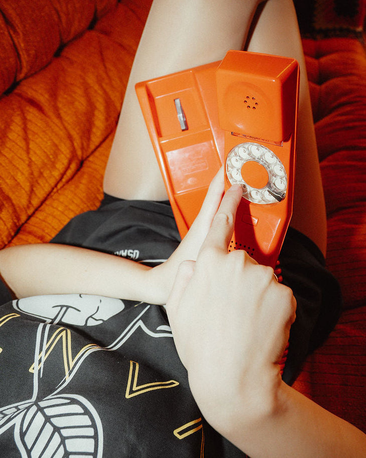 Person holding a retro orange telephone against a red couch.