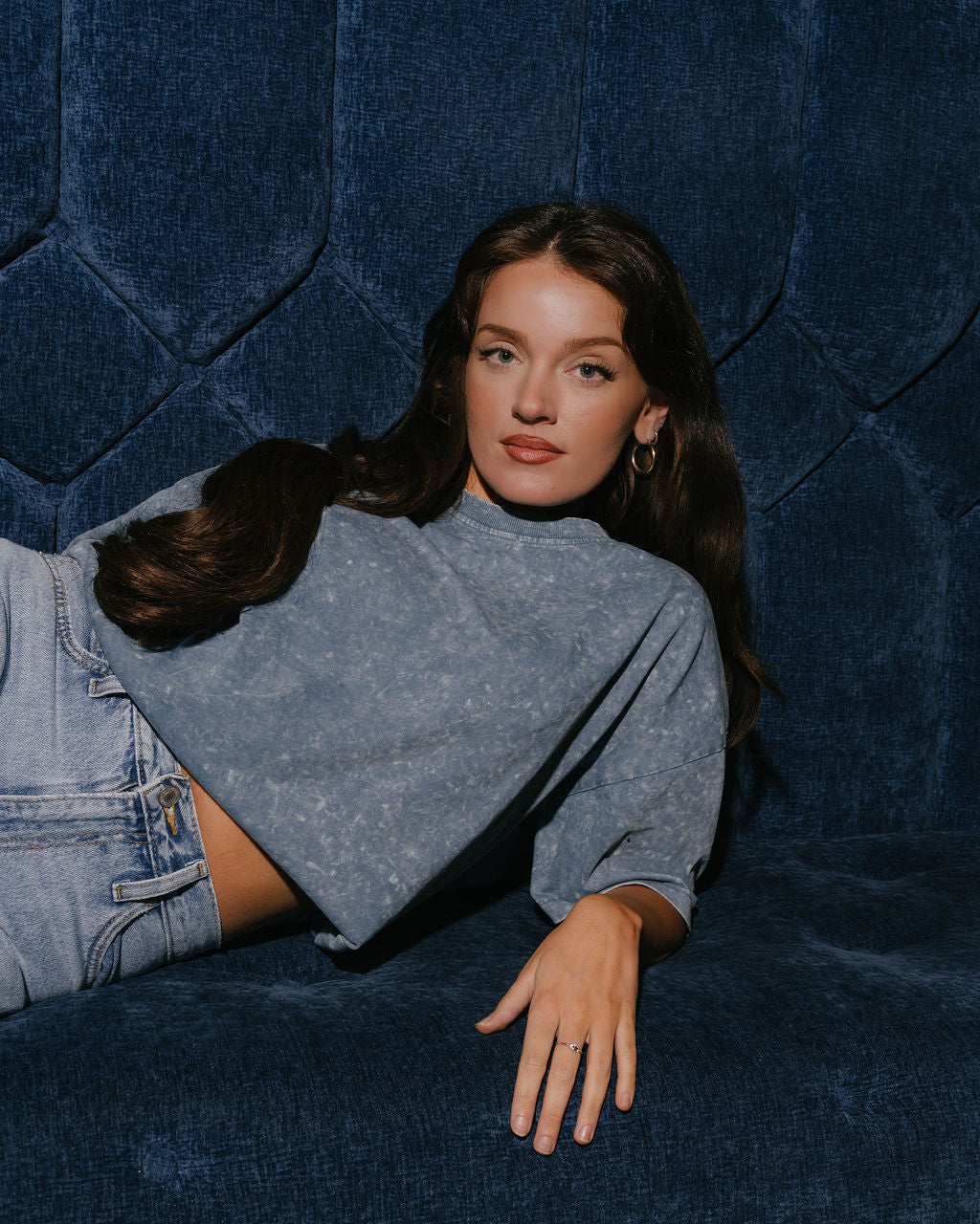Woman lying on a blue textured surface wearing a gray sweater and denim shorts.