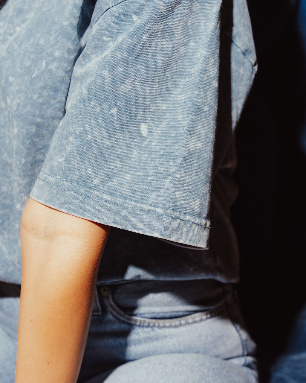 Close-up of a person wearing a blue denim shirt and jeans.